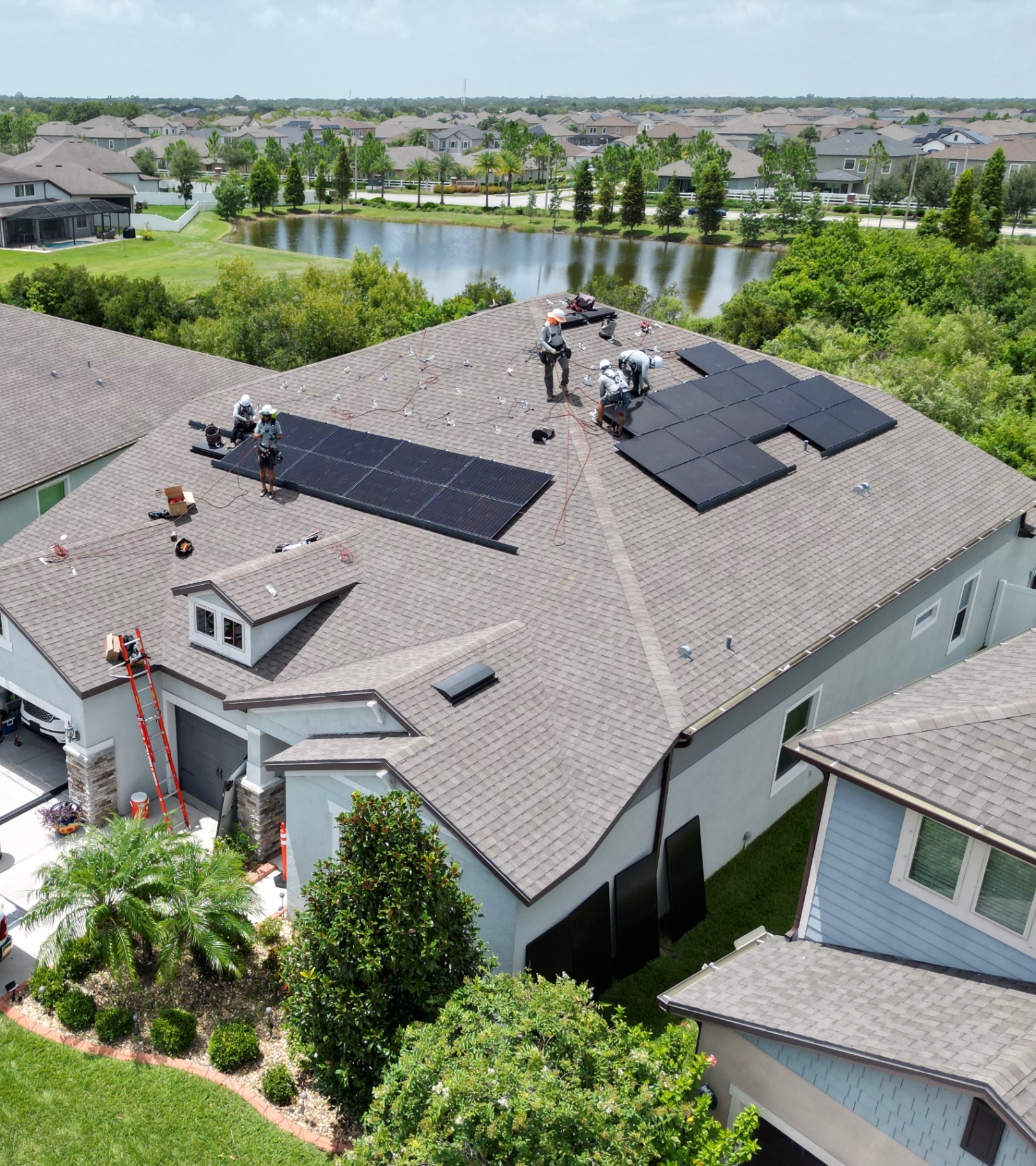 Installation crew securing mounting rails and black solar panels on a residential shingle roof
