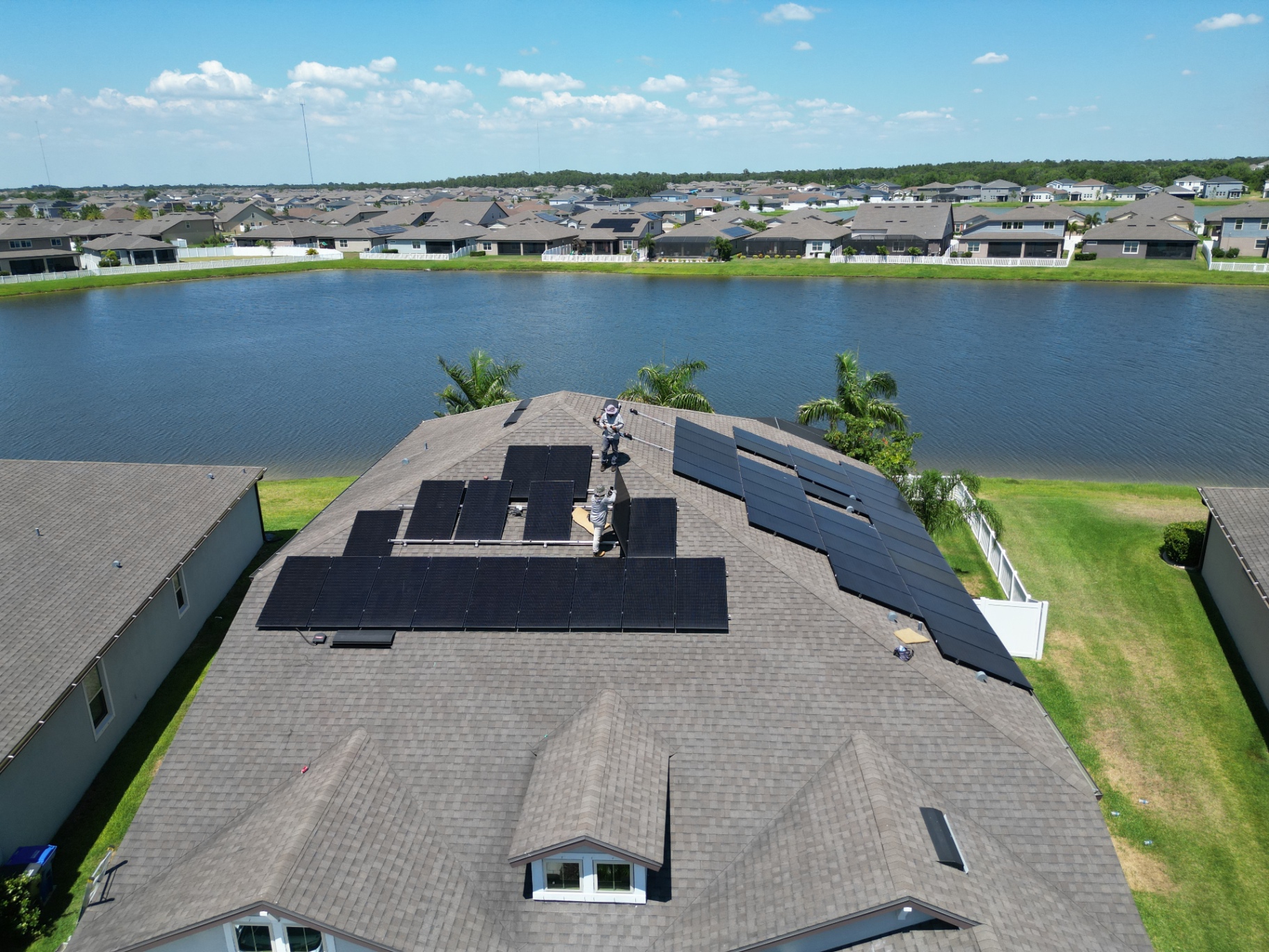 Aerial view of an active residential solar installation on a Florida home overlooking a neighborhood lake