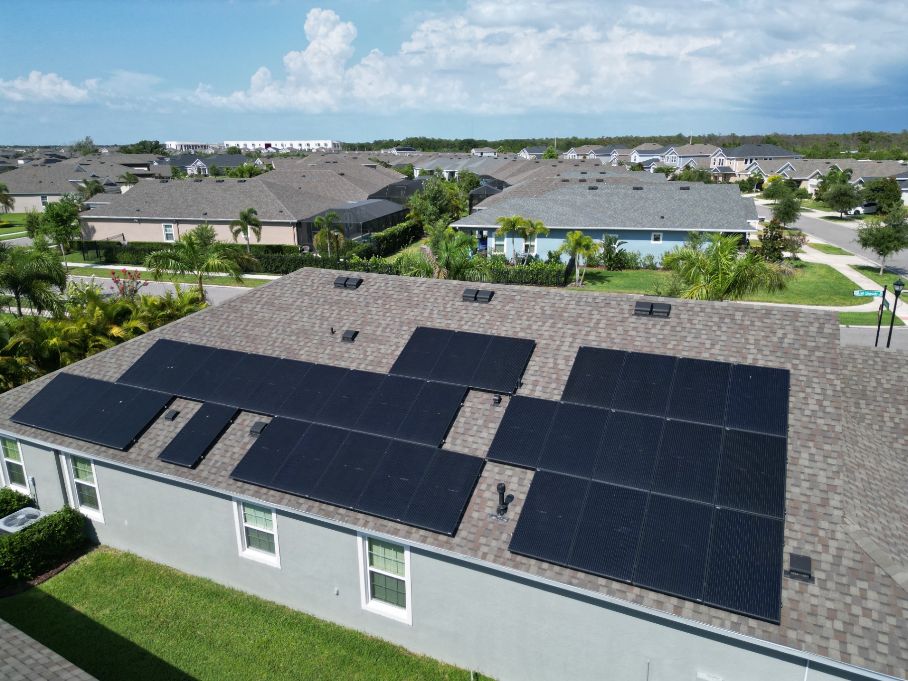 Aerial view of a completed black solar array laid out across the roof planes of a single-story home